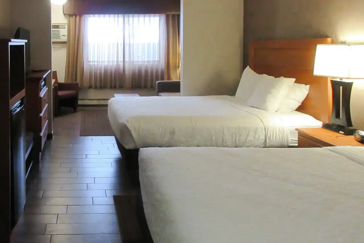 A guest room at The DL Hotel with two queen beds, a curtained window and a bedside lamp