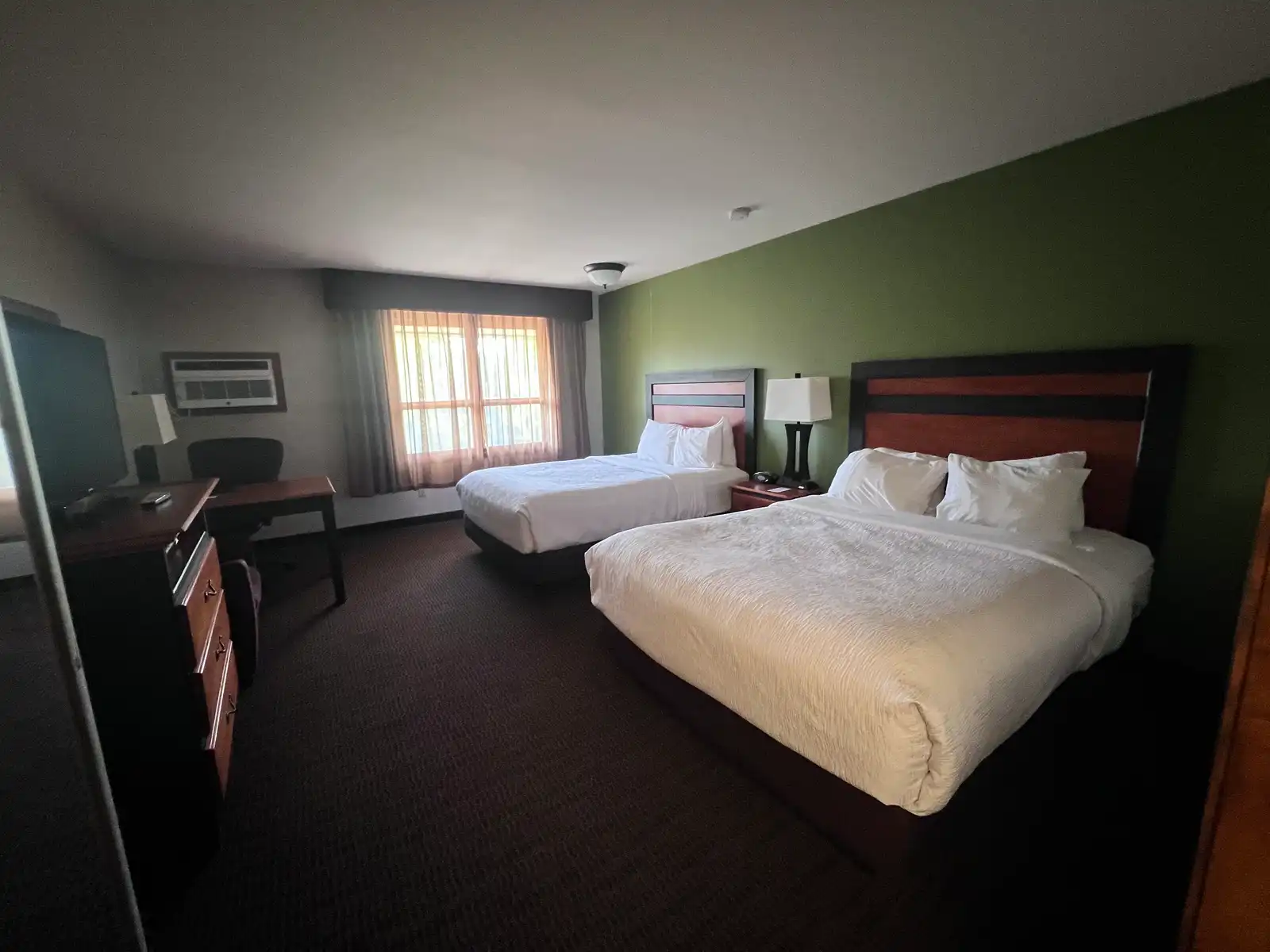 A two queen room with a green feature wall, a desk by the window and a flat-screen TV
