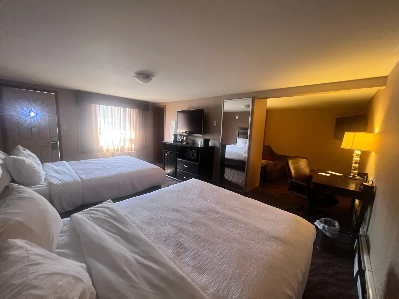 A two queen suite with a mirrored wall, a fridge and microwave counter and a desk by the window